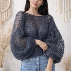 Puede incluir: Un suéter azul oscuro transparente con cuello barco y mangas voluminosas. El suéter se combina con vaqueros de mezclilla azul claro. El estilo general es casual y cómodo, adecuado para el uso diario. La textura del suéter parece suave y aireada.