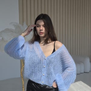 May include: A light blue knitted cardigan with pearl buttons and a V-neck. The cardigan has a loose fit and long sleeves.