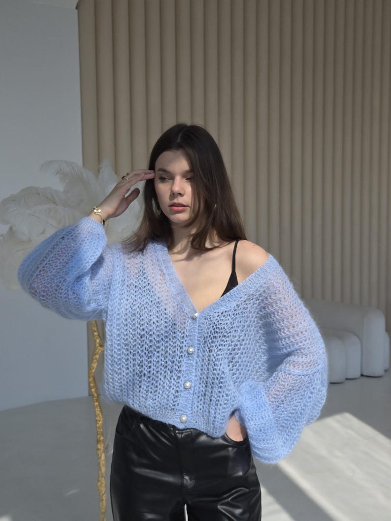 May include: A light blue knitted cardigan with pearl buttons and a V-neck. The cardigan has a loose fit and long sleeves.