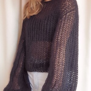 May include: A black, sheer, knitted sweater with long, puffed sleeves. The sweater is loose-fitting and cropped.