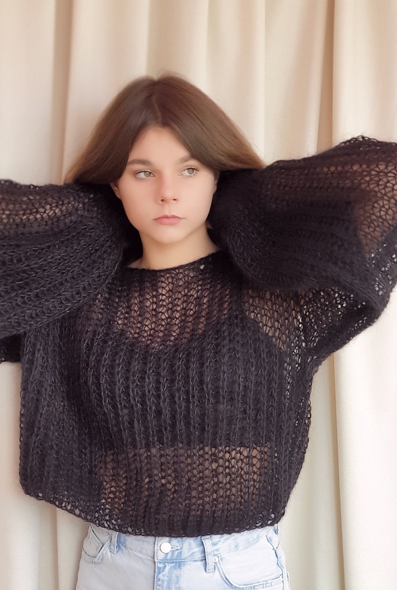 May include: A black, sheer, knitted sweater with a loose fit and long sleeves. The sweater is made of a soft, lightweight yarn and has a relaxed, casual style.