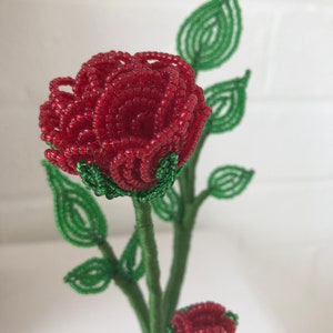 May include: A beaded rose bouquet with two red roses and green leaves. The roses are made of small red beads and the leaves are made of green beads.