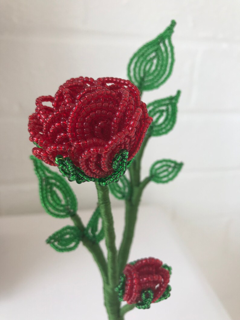 May include: A beaded rose bouquet with two red roses and green leaves. The roses are made of small red beads and the leaves are made of green beads.