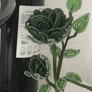 May include: A beaded green rose with a stem and leaves. The rose is made of small, round beads that are strung together to create a realistic-looking flower.