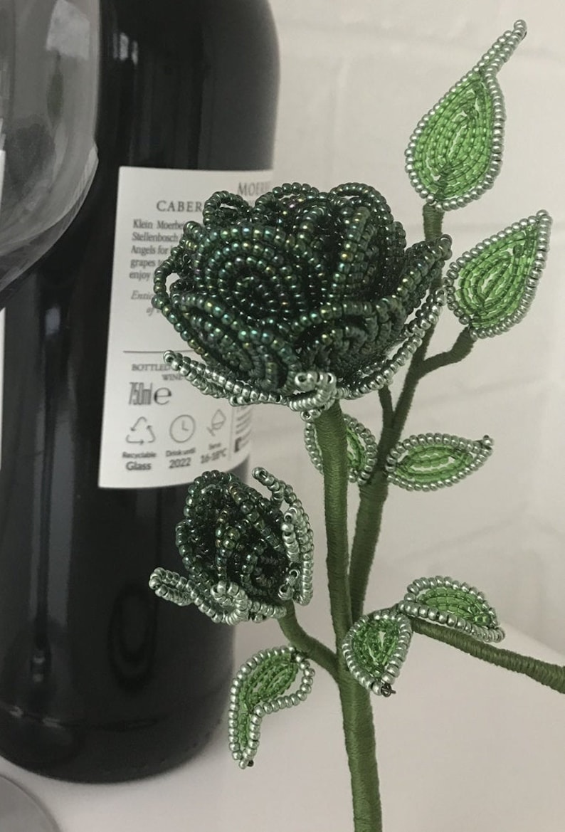 May include: A beaded green rose with a stem and leaves. The rose is made of small, round beads that are strung together to create a realistic-looking flower.