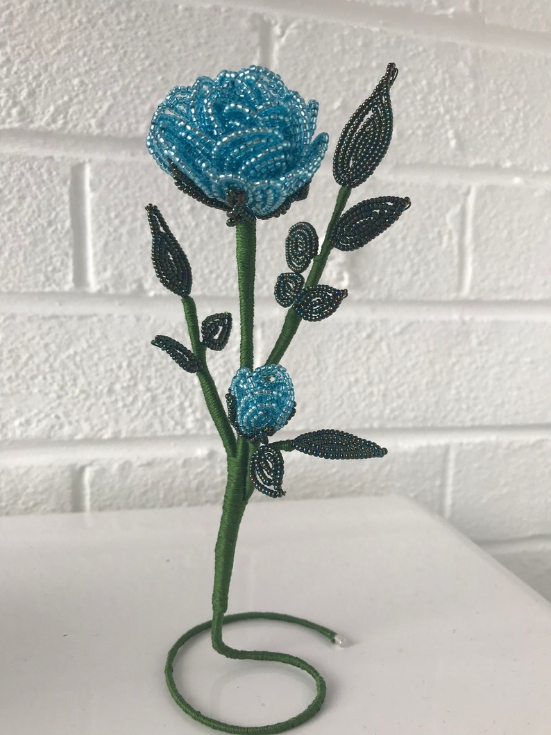 May include: A blue beaded rose with green beaded leaves and stem, standing on a green wire base.