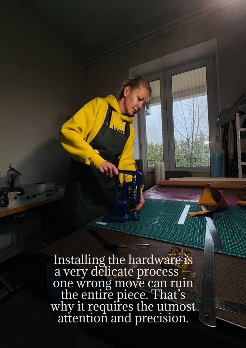 May include: A person in a yellow hoodie and black apron uses a blue press to install hardware on a leather project. The text in the image reads: "Installing the hardware is a very delicate process..."
