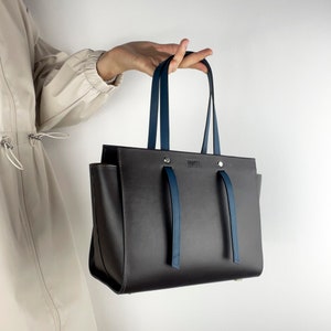 May include: A dark brown leather tote bag with blue leather straps and a silver metal logo that says "BY FAR".