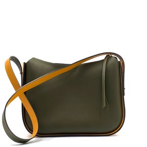 May include: An olive green shoulder bag with a mustard yellow strap. The bag has a minimalist design with a curved shape and a small logo. The strap is adjustable and the bag appears to be made of leather or a similar material. The bag's dimensions are approximately 30 cm in length.