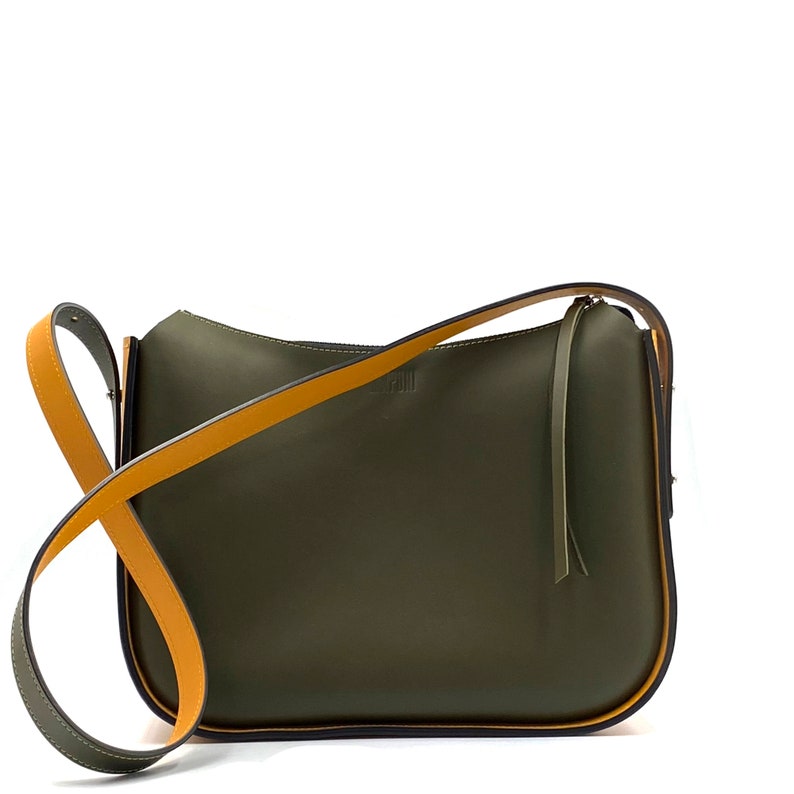 May include: An olive green shoulder bag with a mustard yellow strap. The bag has a minimalist design with a curved shape and a small logo. The strap is adjustable and the bag appears to be made of leather or a similar material. The bag's dimensions are approximately 30 cm in length.