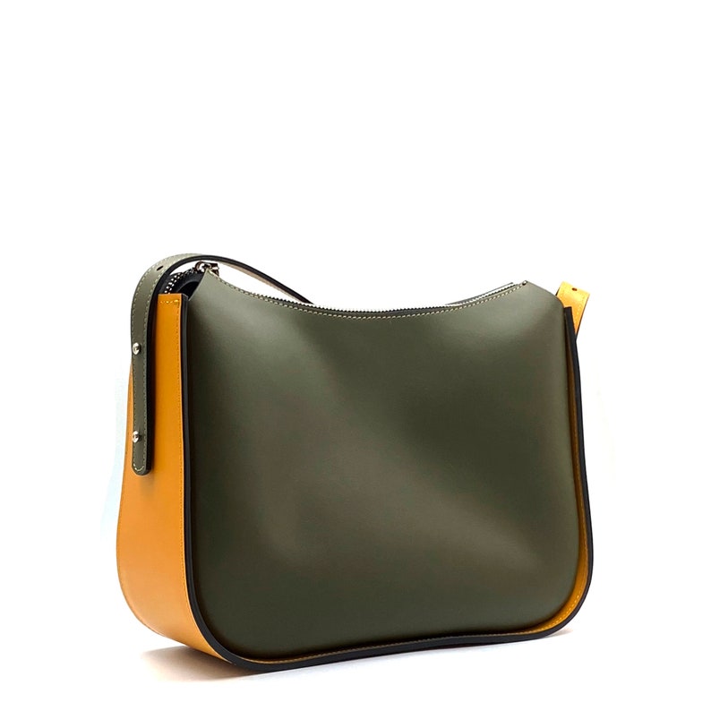 May include: Olive green shoulder bag with a curved top and a zip closure. The bag has a mustard yellow accent on the side and strap. The bag is made of a smooth material.