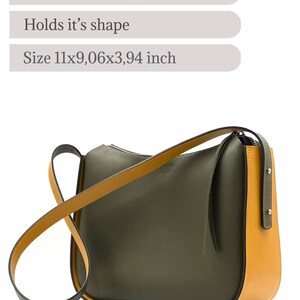May include: A stylish olive green and mustard yellow leather shoulder bag. It has a curved design, a long strap, and steel hardware. Made from genuine Italian leather, the bag measures approximately 28x23x10 cm.