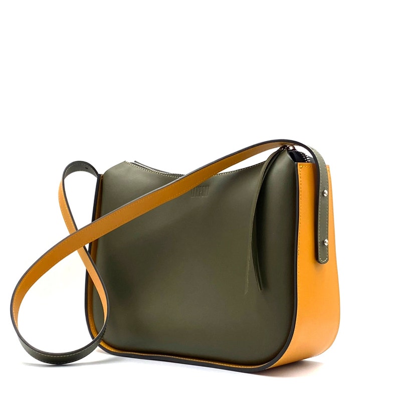 May include: Olive green and mustard yellow shoulder bag with a long strap. The bag has a curved shape and a zip closure. The strap is mustard yellow on one side and black on the other. The bag has the word "LIFEN" printed on it.