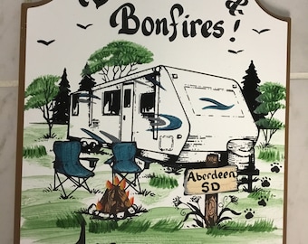 May include: A white wooden sign with a brown border, featuring a hand-painted illustration of a camper, two chairs, and a campfire. The sign reads "Burgers, Beer & Bonfires!" and "Jason and Tracy" with a signpost that says "Aberdeen SD".