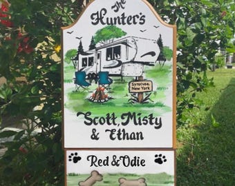 May include: A wooden sign with a hand-painted illustration of a camper, a campfire, and two chairs. The sign reads "The Hunter's", "Scott, Misty & Ethan", "Red & Odie", and "Syracuse, New York".
