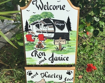 May include: Welcome sign with a painted image of a camper, a campfire, and two red chairs. The sign reads "Welcome", "Ron and Janice", and "and Harley too!" with two bone icons.