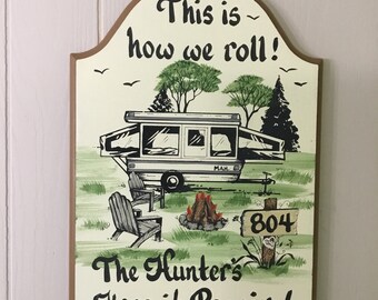 May include: A wooden sign with a hand-painted illustration of a camper van, trees, and a campfire. The sign reads "This is how we roll! The Hunter's Keep it Poppin!" and has a house number sign that reads "804".