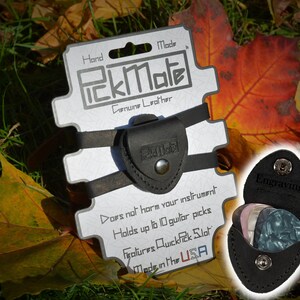 K&ouml;nnte beinhalten: Schwarzer Leder-PickMate-Gitarrenplektrumhalter mit dem Text "PickMate" und "Genuine Leather". Der Halter ist an einer wei&szlig;en Karte mit dem Text "Made in the USA" befestigt. Der Halter kann bis zu 10 Gitarrenplektren aufnehmen.