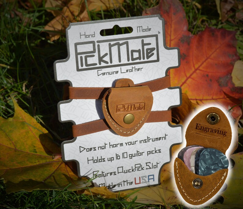 K&ouml;nnte beinhalten: Ein brauner PickMate Gitarrenplektrumhalter aus Leder mit dem Text "PickMate" und "Genuine Leather". Der Halter ist an einer wei&szlig;en Karte mit dem Text "Hand Made" und "Made in the USA" befestigt. Der Halter kann bis zu 10 Gitarrenplektren aufnehmen.