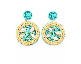 May include: A pair of turquoise beaded earrings with a circular design. The earrings feature a woven, light brown border, turquoise beaded center, and small seashells. The top of the earrings are turquoise beaded circles.