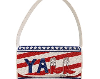 May include: A beaded clutch with a white handle. The clutch features a red and white striped pattern with blue stars and the word "Y'ALL" in blue. Cowboy boots are also featured on the clutch.