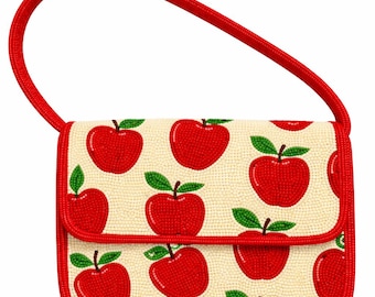 May include: A small, rectangular handbag with a red handle and trim. The bag features a cream-colored background covered in a pattern of red apples with green leaves. The handle is a thick, twisted red cord.