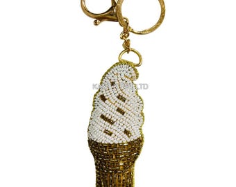 May include: A gold-colored keychain featuring a beaded ice cream cone design. The ice cream cone has a brown base and a white top with brown accents. The keychain includes a clasp and a ring for attaching keys.