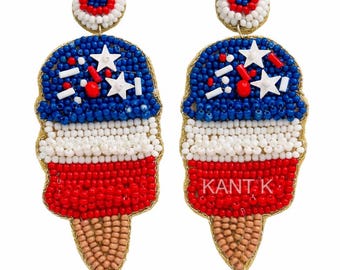 May include: A pair of beaded ice cream cone earrings in red, white, and blue. The earrings feature a blue top with white stars and sprinkles, a white middle section, and a red bottom. The cone is tan, and the earrings have a gold border.