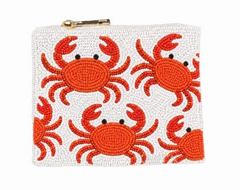 May include: White beaded clutch with a repeating pattern of orange crabs. The crabs have black eyes and are evenly spaced across the surface. A gold zipper closure is at the top.