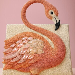 May include: A beaded flamingo-shaped clutch in shades of orange, peach, and cream. The flamingo features a black beak, a curved neck, and a body adorned with pink gemstone accents. The rectangular clutch has a textured, cream-colored base.