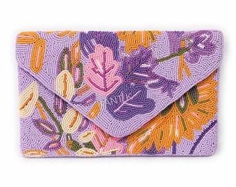 May include: A beaded clutch in shades of lavender, orange, pink, and green. The clutch features a floral design with leaves and flowers. The word "ANTIK" is visible on the flap. The clutch is rectangular with a flap closure.