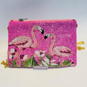 May include: Pink beaded clutch featuring two flamingo designs with white and pink details, surrounded by floral and leaf accents. The clutch has a zipper closure and a gold chain strap. The text "KANTIK" is visible on the clutch.