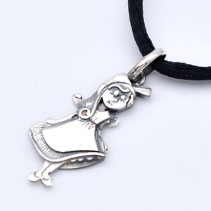 May include: A silver pendant in the shape of a cartoon girl, with a smiling face and a dress. The pendant is attached to a black cord. The girl pendant is a charming accessory.