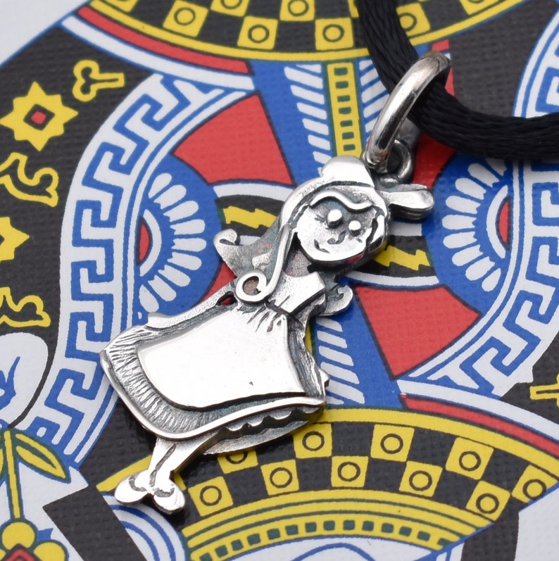 May include: A silver pendant necklace featuring a stylized figure of a girl in a dress and bonnet. The pendant is suspended from a black cord. The background is a colorful playing card design.