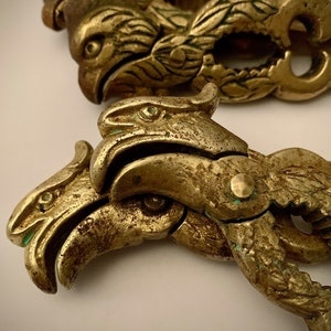 May include: Two antique brass nutcrackers, each featuring a detailed eagle head design. The nutcrackers are a tarnished gold color, showing signs of age and use. The eagle's beaks form the cracking mechanism.