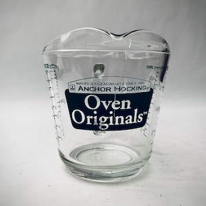 May include: A clear glass measuring cup with a blue and white label that reads "America's Glassmaker Since 1905 Anchor Hocking Oven Originals".
