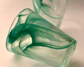 Puede incluir: Dos vasos para beber de vidrio transparente con un diseño verde en espiral. Los vasos están apilados uno encima del otro.