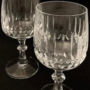 Puede incluir: Dos copas de vino de cristal transparente con un diseño de cristal tallado. Las copas tienen un tallo alto y delgado y una copa redonda.