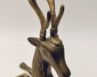 May include: A gold-coloured brass deer figurine with detailed antlers and a lying down pose.