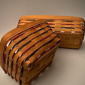 May include: Two woven baskets with red, black and green trim. The baskets are made of natural wood and have a rectangular shape.