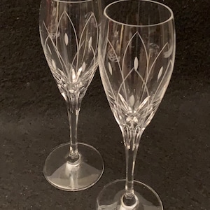 Può includere: Due flute da champagne in vetro trasparente con motivi floreali incisi. Le flute hanno un gambo alto e sottile e una coppa larga e rotonda.