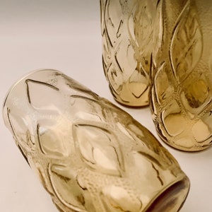 May include: Four amber glass tumblers with a diamond pattern. The glasses are stacked on top of each other.