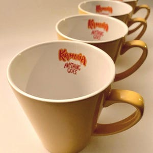 May include: Set of five yellow ceramic mugs with white interiors. Each mug features the Kahlua logo and the text "Anything Goes".