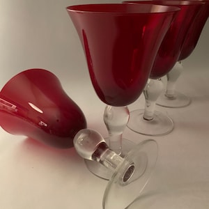 May include: Set of four red wine glasses with clear glass stems and bases. The glasses have a wide bowl and a delicate, elegant design.