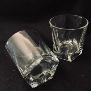 Puede incluir: Dos vasos transparentes de vidrio con forma hexagonal. Los vasos están vacíos y se encuentran sobre una superficie negra.