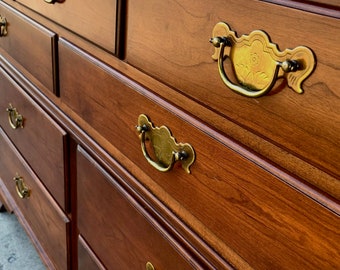 May include: A wooden dresser with six drawers and ornate brass handles. The dresser is made of a rich, dark wood with a warm, natural finish.