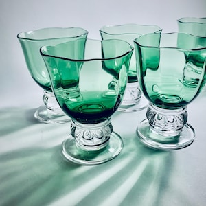 Può includere: Set di quattro calici in vetro verde con steli e basi in vetro trasparente. I calici hanno un bordo ondulato unico e una coppa leggermente svasata.