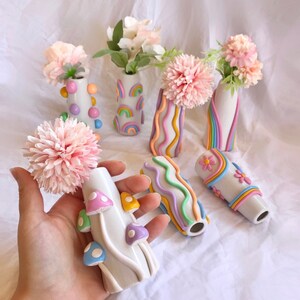 May include: A set of seven colorful ceramic vases with rainbow designs. The vases are decorated with flowers and are arranged on a white surface.