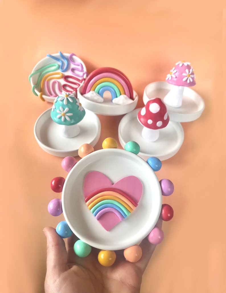 Puede incluir: Un conjunto de cinco platos de anillo de cer&aacute;mica coloridos con diferentes dise&ntilde;os. Cada plato presenta un arco&iacute;ris, un coraz&oacute;n con un arco&iacute;ris, un hongo con flores blancas o un dise&ntilde;o de espiral. Los platos son perfectos para guardar anillos, pendientes u otros art&iacute;culos peque&ntilde;os.