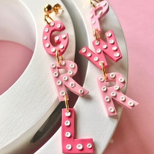 May include: Pink and white polka dot letter earrings spelling out "GIRL".